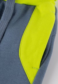 Grauer Hoodie mit neon-gelben Akzenten, ausgestattet mit einem strukturierten Stoff und integrierten Taschendetails auf der linken Seite.