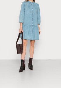 Ljusblå denimklänning med långa puffärmar, knäppning, samlad midja och utsvängd kjol. Matchas med mörkbruna ankelstövlar och väska.