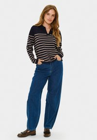 Czarny i beżowy sweter w paski z kołnierzykiem, w zestawieniu z granatowymi dżinsami o wysokim stanie i szerokimi nogawkami oraz ciemnymi mokasynami.