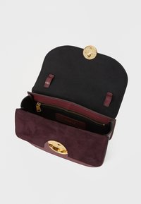 Borsa in suede bordeaux con interno nero. Presenta una chiusura rotonda in oro, una tasca con zip e una texture liscia. Il design aperto mette in mostra i vari scomparti.