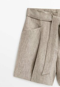 Pantaloni beige in lino a vita alta, con una larga cintura di stoffa legata in vita e ampie tasche frontali.