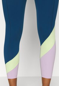 Vysoké legíny v tmavě modré barvě se světle zelenými a levandulovými diagonálními panely. Hladká, elastická tkanina s kontrastními švy.