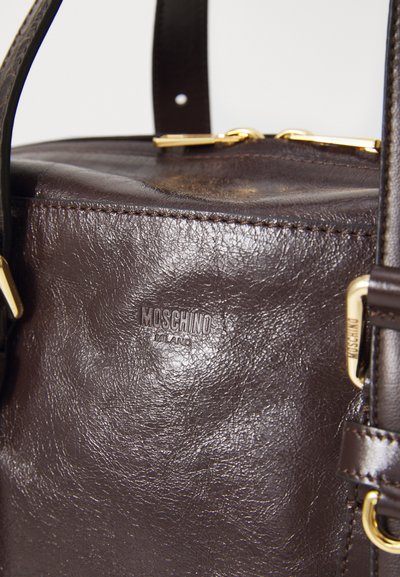 Braune Lederhandtasche mit strukturiertem Oberflächen, ausgestattet mit goldenen Hardware-Akzenten und einem sichtbaren Logo, zylindrischer Form und kurzen Griffen.