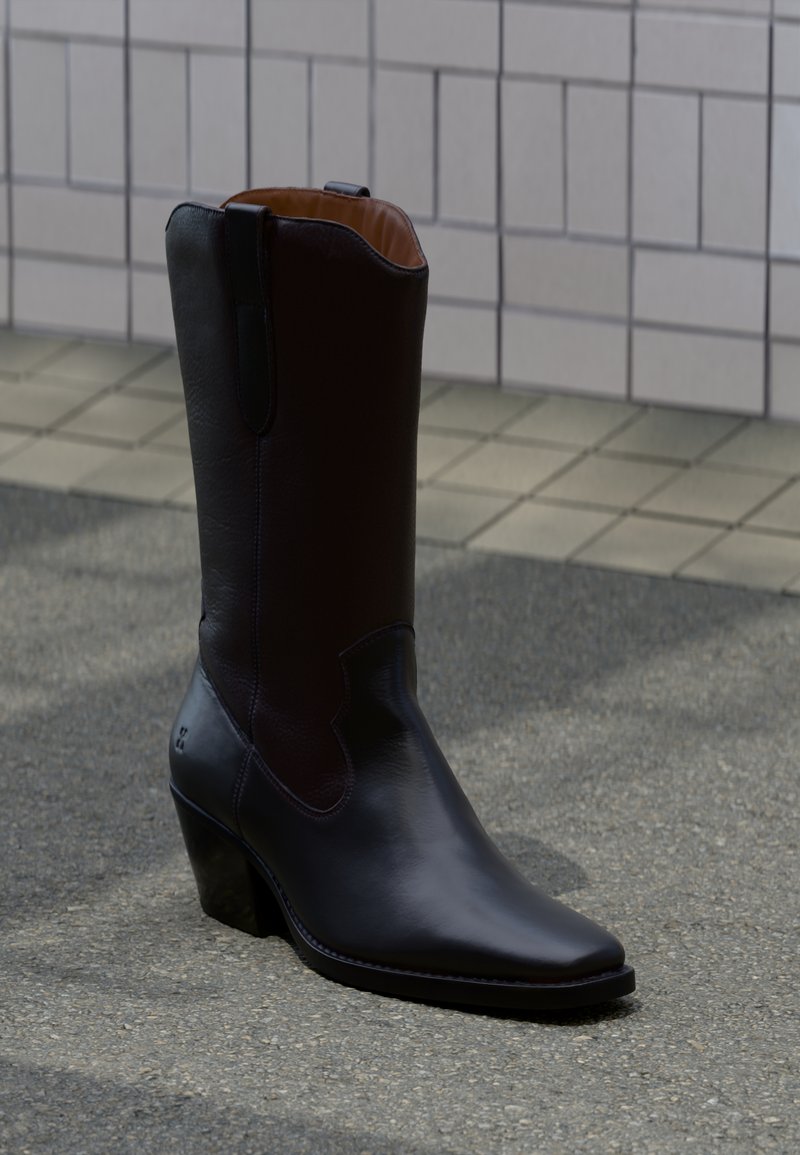 Υψηλή μαύρη δερμάτινη καουμπόικη μπότα με μυτερή μύτη και γωνιακή επίπεδη φτέρνα, που στέκεται σε πλακιδωτή και ασφαλτοστρωμένη επιφάνεια.