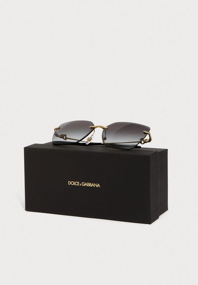 Naočale bez okvira u crnom s gradijentnim staklima s pozlaćenim drškama odmaraju se na crnoj kutiji Dolce & Gabbana s pozlaćenim logotipom sprijeda.