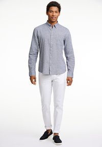 Overhemd met knopen in lichtblauwe stof, met een zak en een kraag, gecombineerd met witte broek en zwarte instappers.