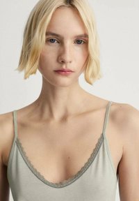 Ljusgrön cami med justerbara band, med en delikat spetsdetalj längs v-ringningen. Slät textur, minimalistisk design.