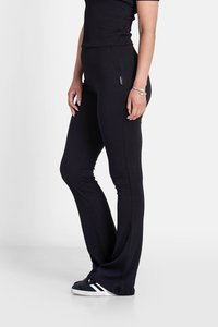 Leggings en tissu noir côtelé avec une taille ajustée, un bas évasé et une branding subtil sur le côté ; accompagnés de baskets noires avec des rayures blanches.