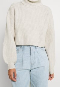 Off-white ribbad stickad polokrage tröja med ballongsärmar, ihop med högmidjade ljusblå denimjeans.