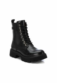Botas de piel negra hasta el tobillo con una suela gruesa negra, con cordones en la parte delantera y ojales de tono dorado. Incluyen una lengüeta en la parte trasera para facilitar su uso.