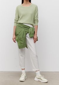 Lichtgroene geribbelde trui, witte broek en een groene jas om de taille gebonden. Sneakers in crème en groen maken de outfit compleet.