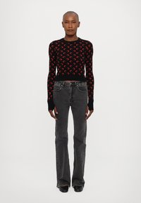 Černý svetr s červenými měsíčními vzory, kombinovaný se šedými zvonovými džíny. Hladká textura materiálu, přiléhavý střih a jemné detaily na džínech.