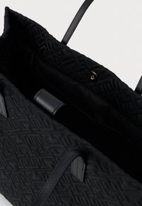 Czarna torba tote o pikowanej fakturze z geometrycznym wzorem, z skórzanymi uchwytami i złotym zapięciem na zatrzask. Przestronne wnętrze, w pełni wyłożone.