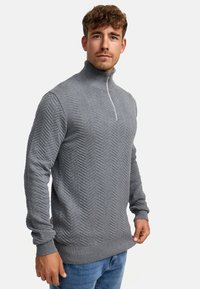 Pulover gri cu fermoar, cu un model texturat de herringbone, cu manșete și curea ribate. Dispune de un guler înalt și un fermoar subtil în față.
