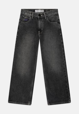 Plati džinsai tamsiai pilkame džinsiniame audinyje. Su mygtuko uždarymu, priekinėmis kišenėmis ir subtiliu prekinio ženklo ženklu su purpuriniu akcentu kairėje kišenėje.