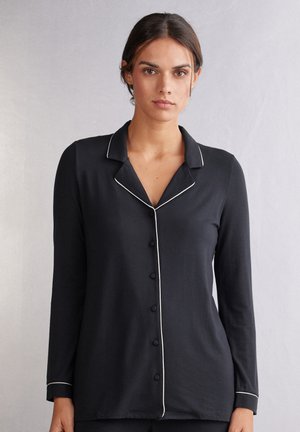 Svart långärmad topp med krage, med vit piping längs kanterna och knappar framtill, tillverkad av ett smidigt material.
