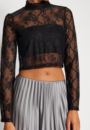 Czarny, długi rękaw, kwiecisty koronkowy crop top noszony z wysokim stanem srebrną plisowaną spódnicą, odsłaniający talię oraz część szyi i rąk.