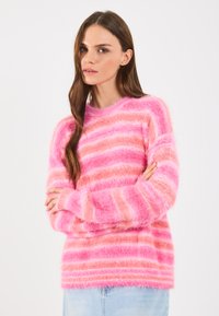 Pulover pufos roz cu dungi orizontale de roz deschis și roz închis, cu guler și manșete ribbate, asortat cu o fustă din denim bleu deschis.