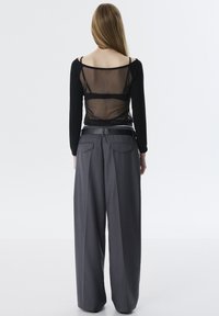 Zwarte langmouwtop met een doorschijnende rug, gecombineerd met grijze wijde broek met een gladde textuur en een riem met een glanzende afwerking.