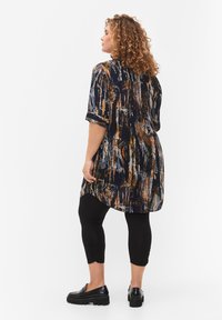 Tunique imprimée à manches courtes de couleur bleu foncé, avec des motifs abstraits orange et blanc. Associée à des leggings noirs et des chaussures noires épaisses.