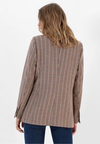 Brun och beige rutigt kavaj med en bakre slits och långa ärmar, i kombination med blå denim. Texturerad tyg med en strukturerad design.