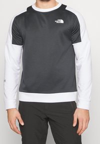 Camicia a maniche lunghe grigia e bianca, con corpo grigio strutturato, maniche bianche lisce, colletto e polsini a costine, e un piccolo logo sul petto.