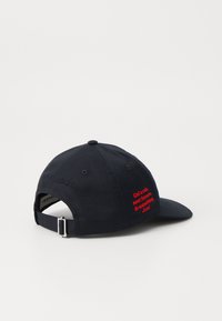 Marineblå baseballcap lavet af bomuld med en buet skygge. Har rød broderet tekst på bagsiden og en metaljusteringsklips.