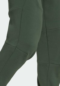 Tmavě zelený sportovní top s texturovanou tkaninou, zdobený výraznými švy a přiléhavým střihem, který zdůrazňuje strukturovaný design.