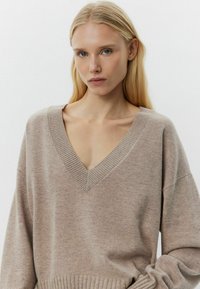 Pulover tricotat bej cu decolteu în V larg și manșete cu model. Prezentare cu o croială lejeră și material texturat. Finisaj neted și aspect moale.