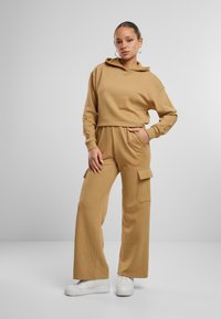 Cropped hoodie marrón combinado con pantalones cargo de pierna ancha que cuentan con bolsillos laterales. El material parece suave y liso, con un corte relajado.