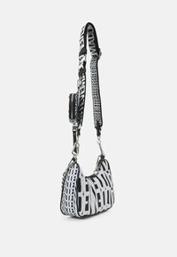 Sac bandoulière noir et blanc avec un grand motif de texte audacieux et une sangle réglable comprenant une petite poche zippée supplémentaire.