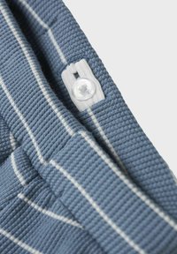 Tessuto blu texturizzato con strisce bianche, con dettaglio di bottone e cuciture. Vista ravvicinata del colletto o dell'orlo di un indumento.