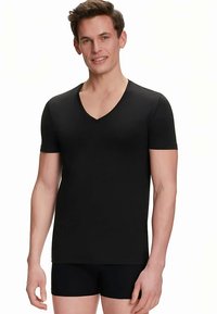 T-shirt nera a maniche corte con scollo a V, dal design aderente e texture liscia, indossata con shorts neri. Estetica pulita e minimalista.