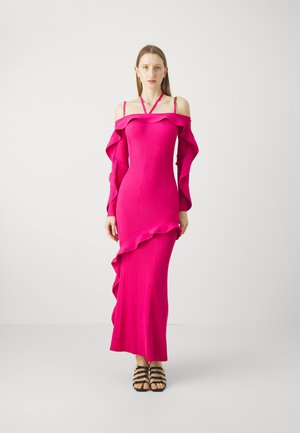 Pink ribbed knit dress with off-shoulder sleeves and ruffled hem detail, long length, paired with black strappy sandals.