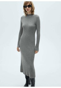 Robe en tricot côtelé gris avec un col haut, des manches longues et une fente sur le côté, assortie à des bottes noires montantes. Tissu lisse et texturé.