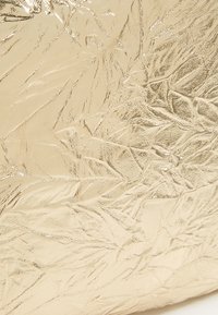 Metaliczny złoty materiał o teksturze z pomarszczonym wzorem, odbijający światło. Powierzchnia wydaje się gładka, z różnym połyskiem i lekkimi wgłębieniami.