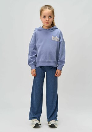 Heled lilla kapuutsiga särk, millel on tekst "feelin' LUCK", paired tekstuursed sinised laiad püksid. Sneakersitel on hõbedane detaile.