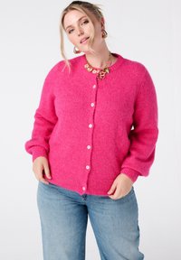 Zachte, felroze cardigan met een ronde halslijn, knoopsluiting en geribbelde manchetten. Gecombineerd met lichtblauwe jeans voor een casual look.