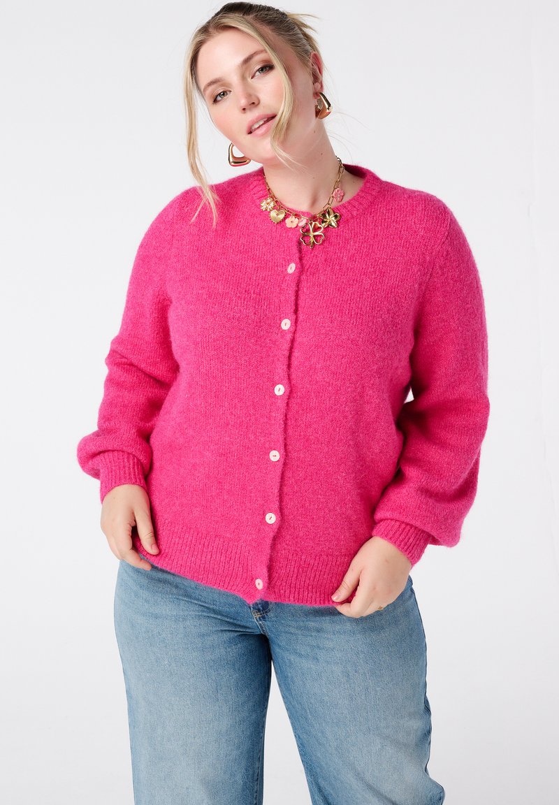 Zachte, felroze cardigan met een ronde halslijn, knoopsluiting en geribbelde manchetten. Gecombineerd met lichtblauwe jeans voor een casual look.