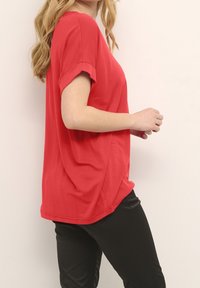 T-shirt rosso a maniche corte realizzato in tessuto morbido, con una vestibilità ampia e maniche arrotolate. Abbinato a pantaloni neri per creare contrasto.