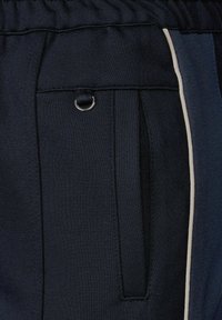 Navy Jogginghose aus strukturiertem Material, mit Seitentasche, elastischem Bund und einer silbernen Metallöse.