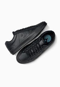 Schwarze Sneaker mit einem glatten Leder-Obermaterial, strukturiertem Nähen, durchbrochenen Akzenten und einer gemusterten Gummisohle. Die Schnürsenkel sind schwarz; die Einlegesohlen haben ein blaues Design.