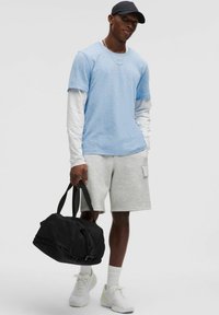 Light blue short-sleeve t-shirt layered over a long-sleeve white shirt, grey shorts, white sneakers, and a black duffle bag.