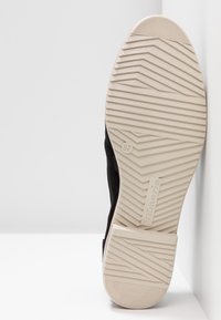Chaussure noire avec tige en suède texturé et semelle en caoutchouc blanche. Dispose d'un motif de bande de roulement en zigzag et d'une taille indiquée comme 37 sur la semelle.