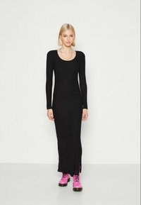 Vestido longo preto canelado de manga longa com decote arredondado e fendas laterais, combinado com botas rosa de atacadores. Textura suave e design justo.