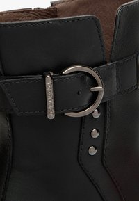 Schwarze Leder-Ankle-Boots mit abgerundeter Spitze, silberner Schnallenakzent und dekorativen Nieten entlang der Seitennaht.