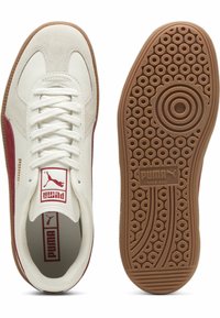 Hvite lær sneakers med røde semskede detaljer, flate hvite lisser og en mønstret gummisåle. Har en Puma-logo på tungen og siden.