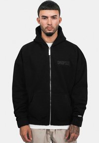 Sort zip-up hoodie lavet af blødt materiale med foret hætte, frontlommer og et lille "DROP-SIZE" logo på brystet.