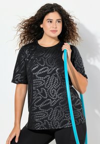 Černé tričko s krátkým rukávem a texturovaným vzorem, vyrobené z lehkého materiálu. Modelka drží tyrkysový hula hoop.