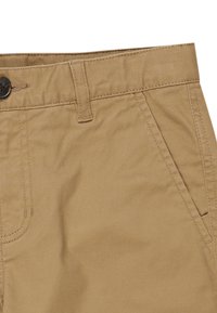 Beige bomulds chinos med en glat overflade, der har en enkelt knaplukning, bæltestropper og skrå sidelommer.